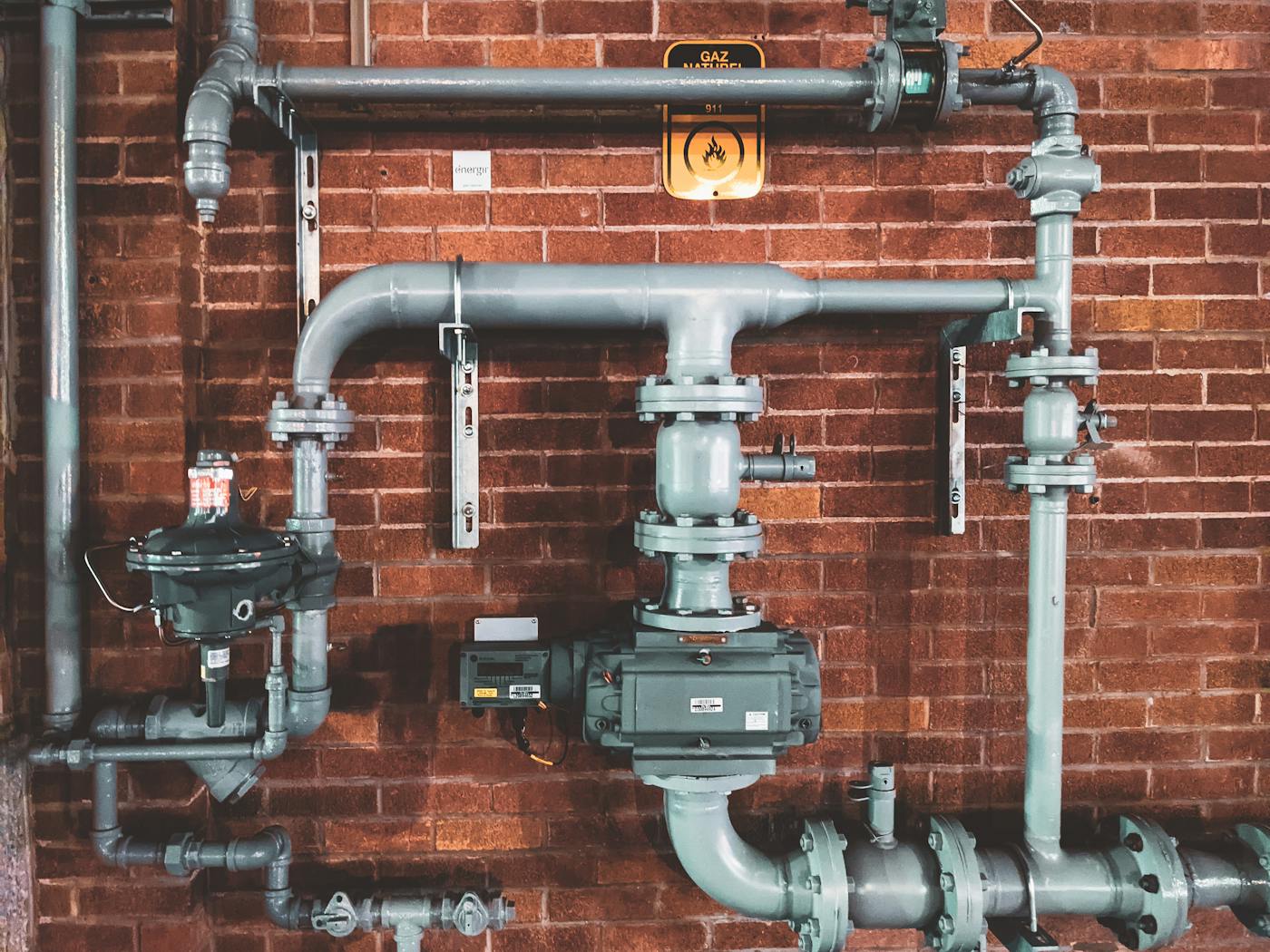 Verzweigte Gas- und Wasserleitungen mit Absperrventilen an einer Backsteinwand